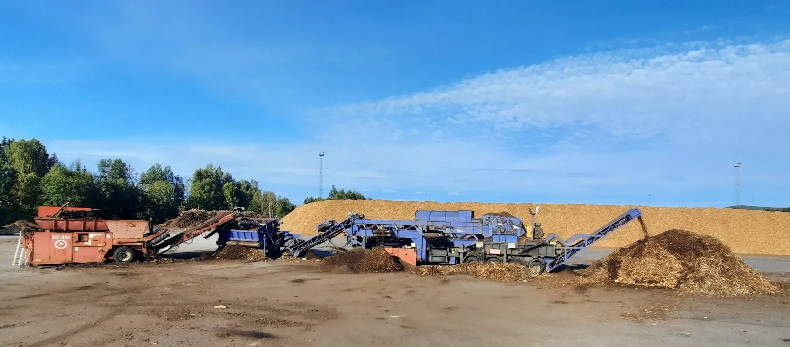 Barkkross och förkross vid stora högar av bark och flis på en industriplan