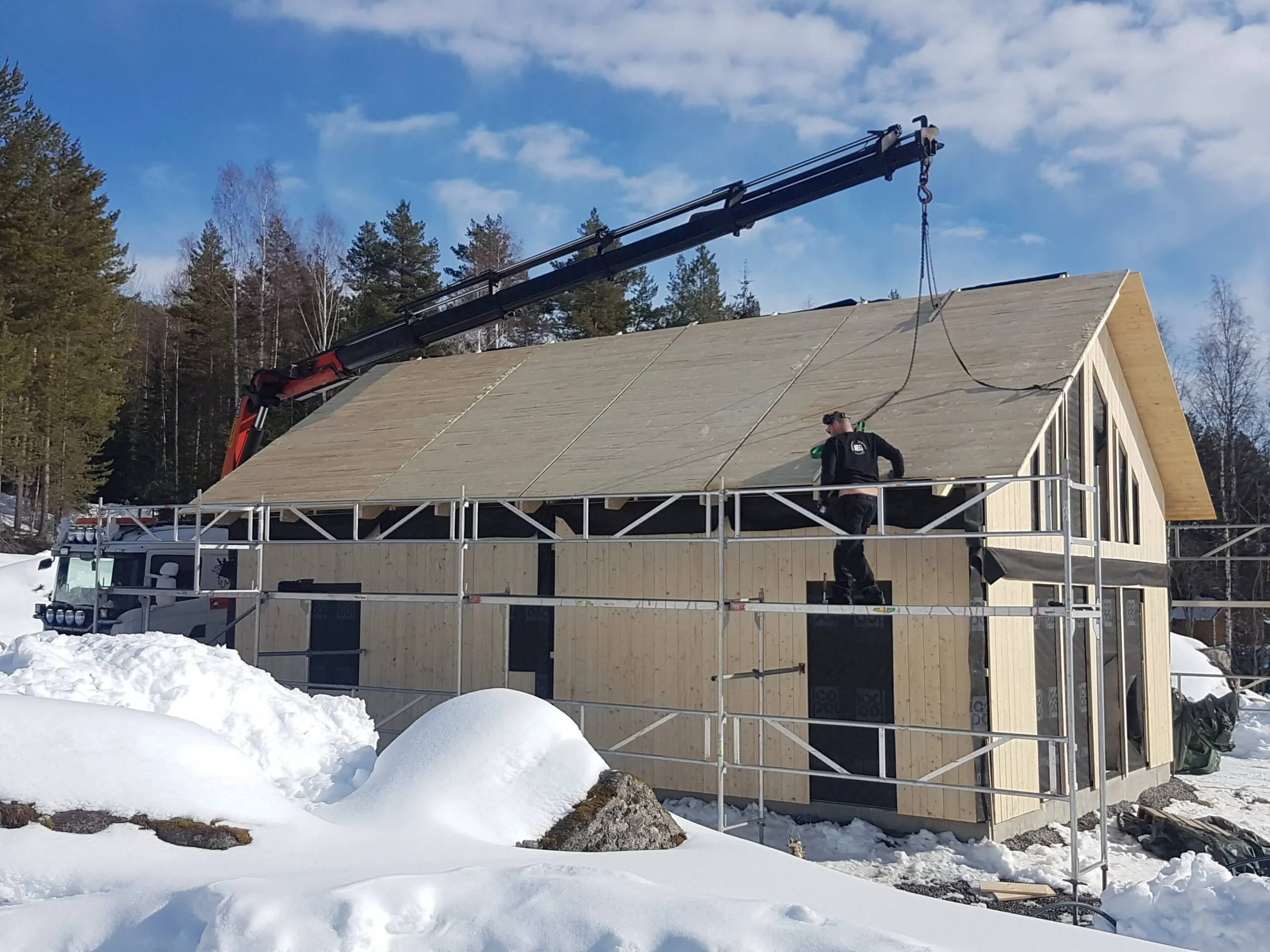 Kranbil lyfter material till taket på ett hus under byggnation