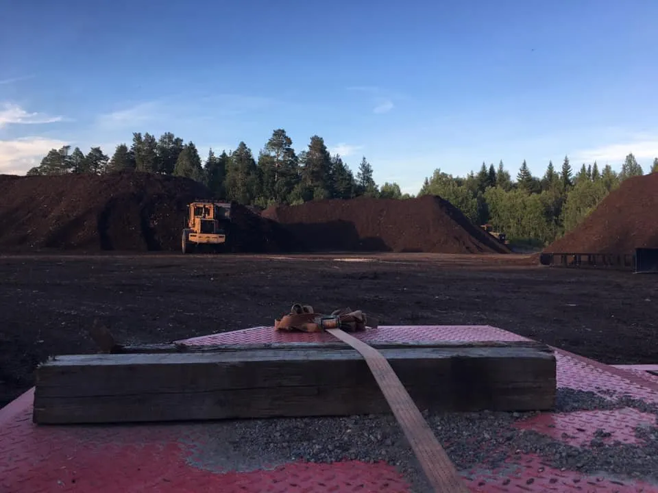 Vy från ett lastbilsflak mot materialhögar och en hjullastare