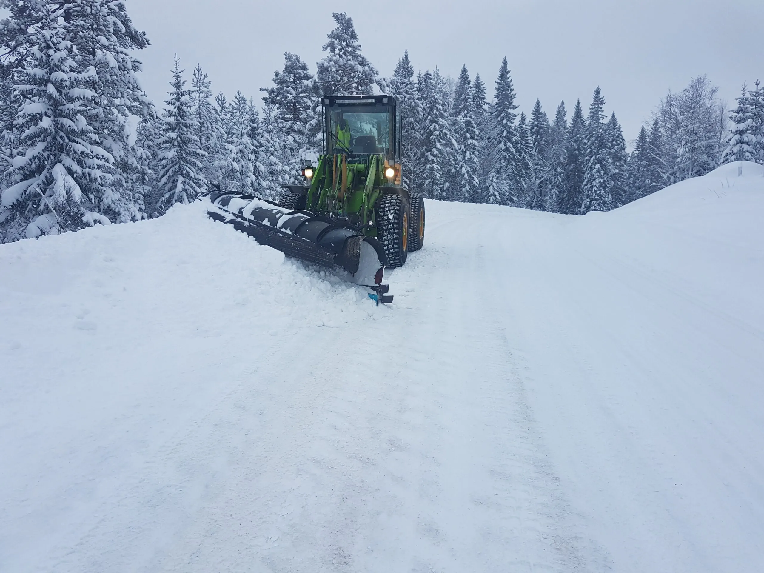 Grön hjullastare med plog på en snöig väg
