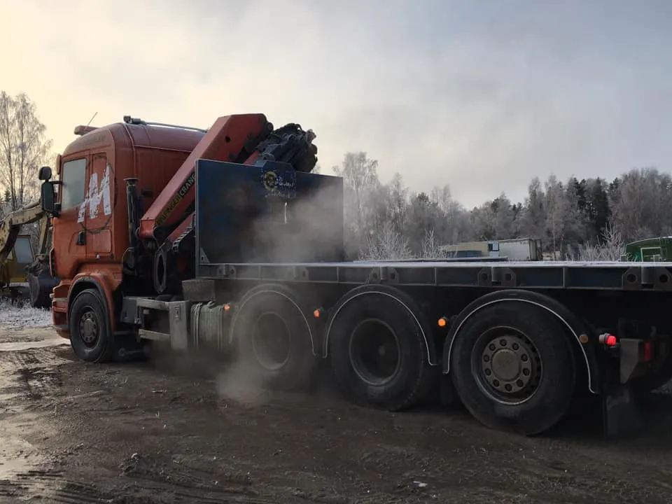 Orange lastbil med kran och flak i vinterväder