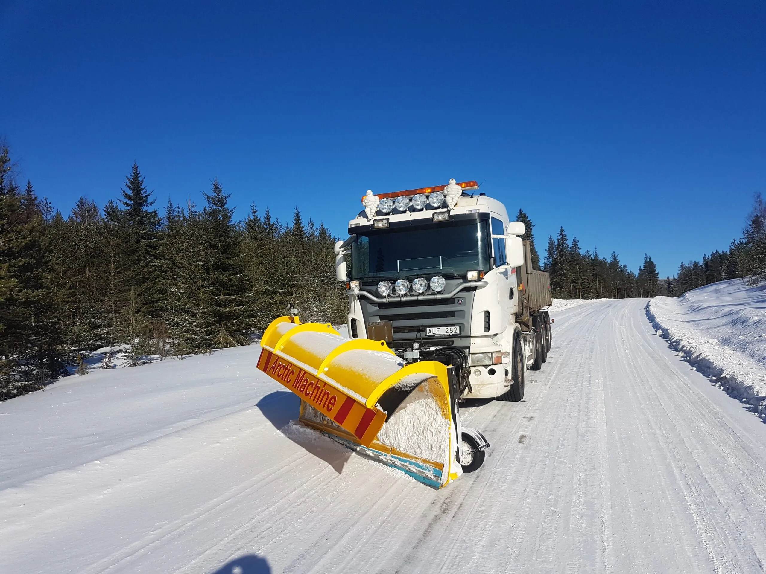 Lastbil med gul plog på en snöig skogsväg