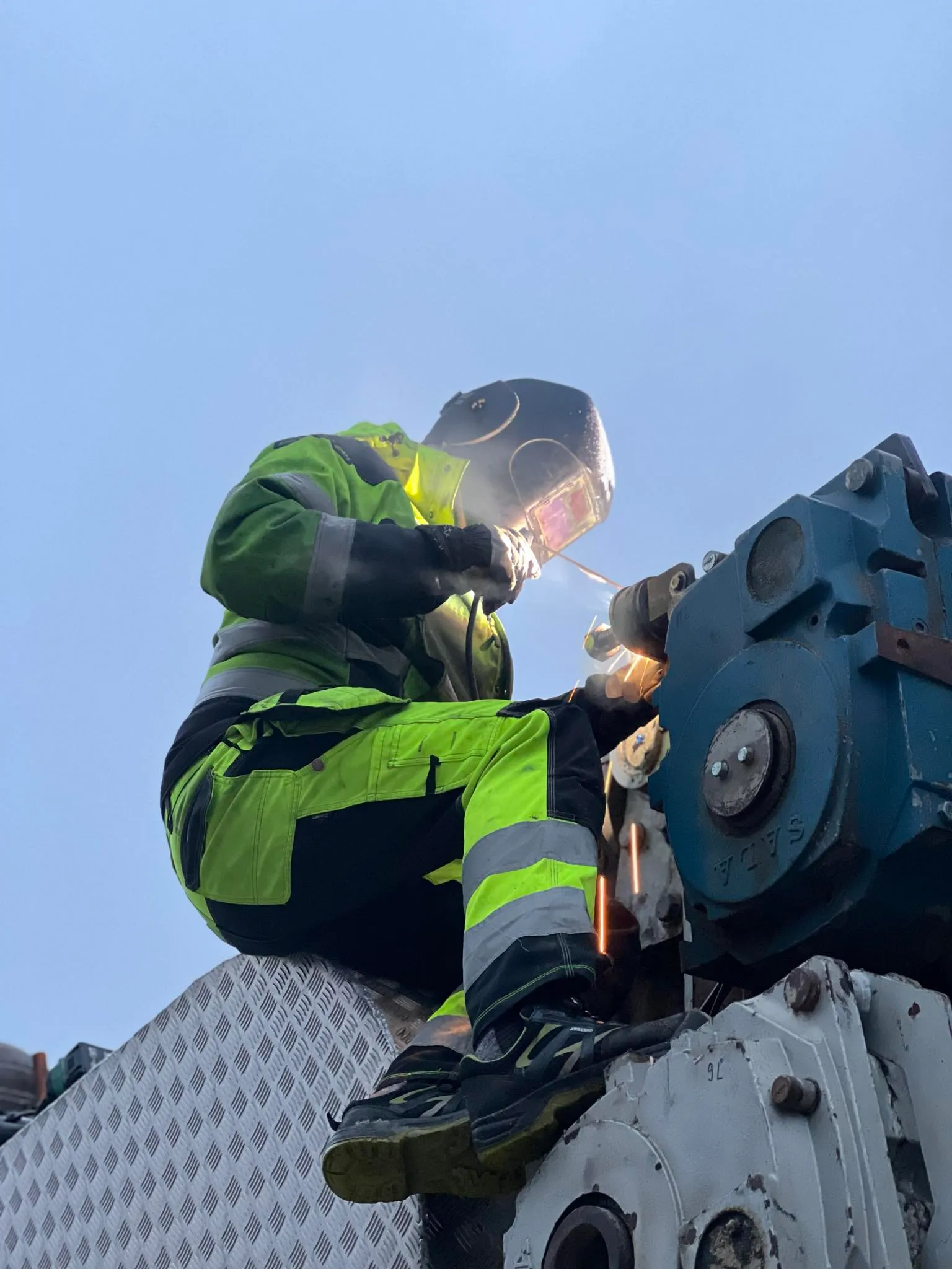 Medarbetare i varselkläder svetsar på en maskin